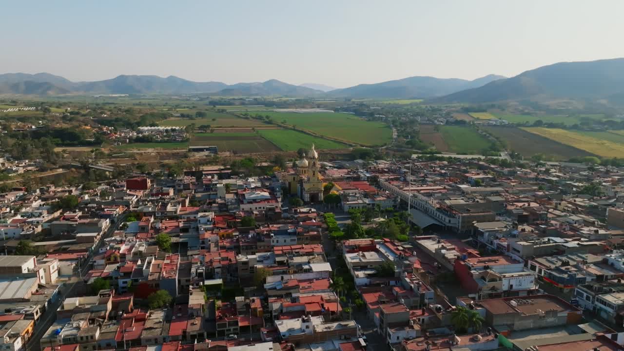 órbita aérea panorámica del centro de la ciudad de tamazula con la iglesia principal, campos agrícolas y montañas lejanas