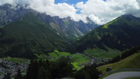 Luftaufnahme-Während-Eines-Drohnenstarts-Von-Einer-Wiese-Mit-Einer-Kurvenreichen-Straße-Und-Hohen-Bergen-Im-Hintergrund,-In-Der-Nähe-Von-Vergoer---Einem-Kleinen-Dorf-Im-Stubaital-In-Österreich