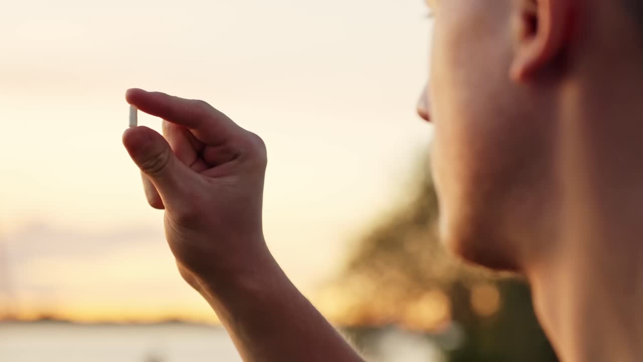 Worker closely inspects small sample jar at sunset evaluating contamination risk near calm water surface