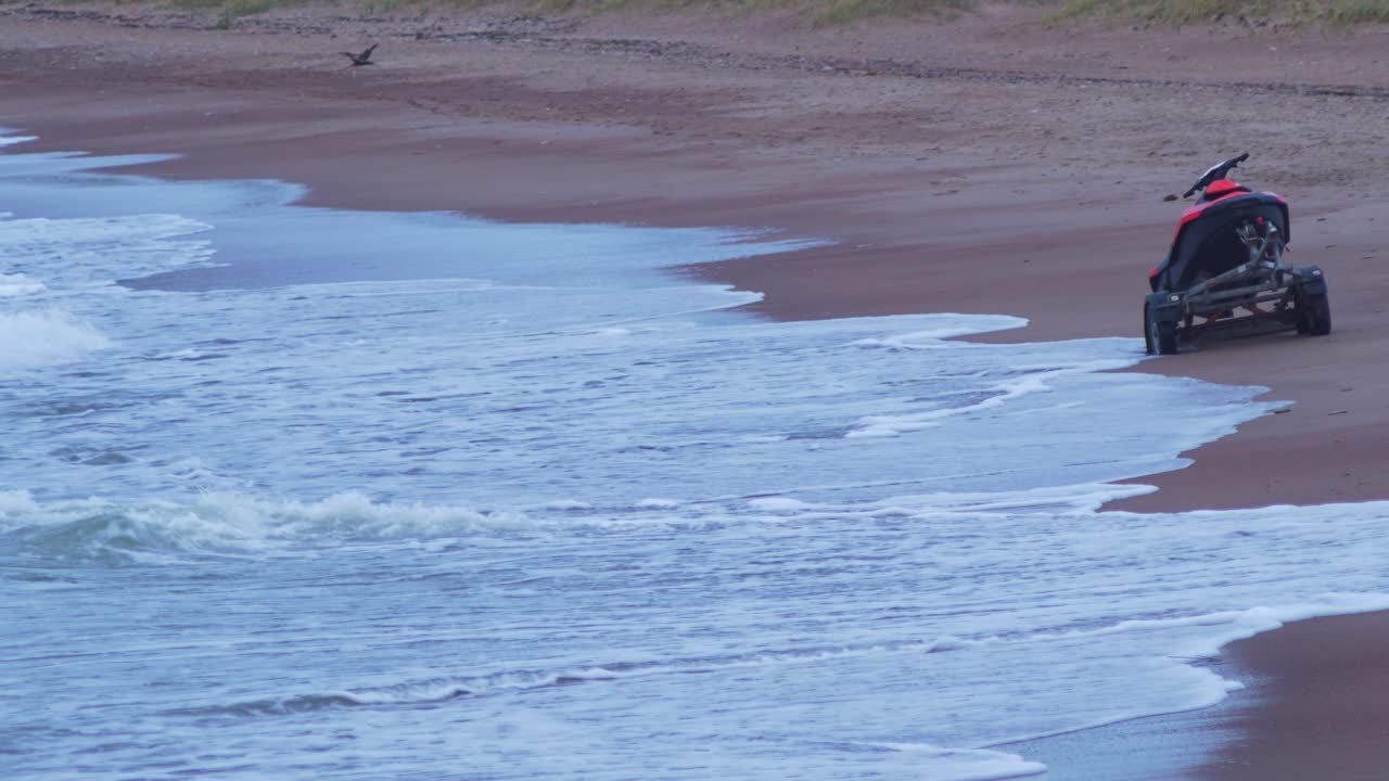 발트해 모래 해변의 트레일러에 있는 레드 제트 스키, 중간 샷