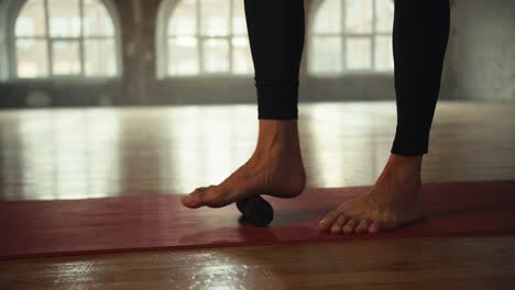 close-up shot of the legs of an athlete who uses a small cone to stretch their feet while standing on the red mat in a sunlit