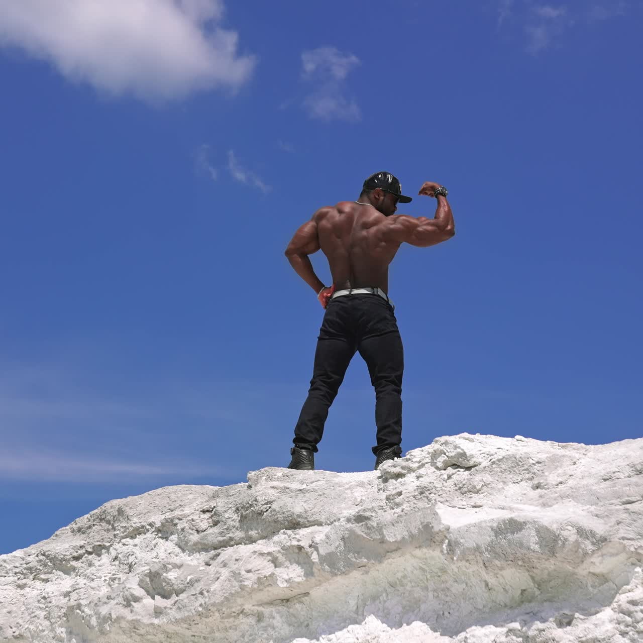 Strong athletic man fitness model. Low angle view of the guy with naked torso showing six pack abs. Clear blue sky on the background