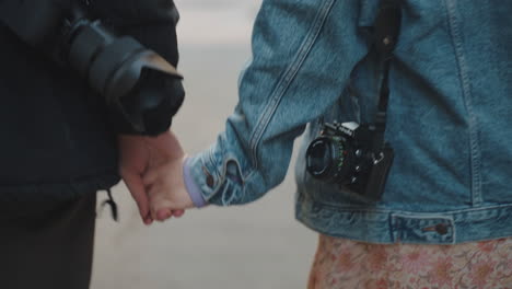 Couple-holding-hands,-cameras-on-shoulders,-exploring-a-urban-setting