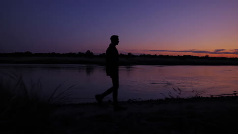 silhouette of a man walking along a river at sunset