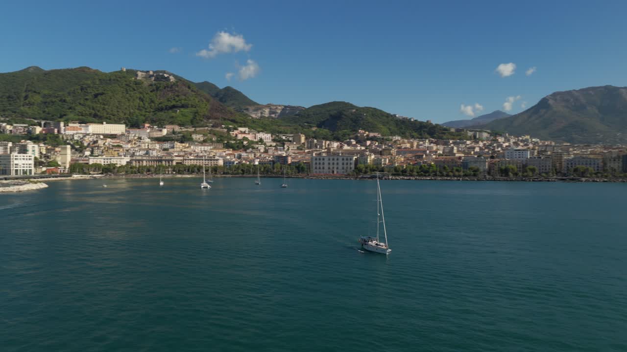 Barca a vela che si allontana dalla città di Salerno in una giornata di sole in Italia. - ripresa aerea