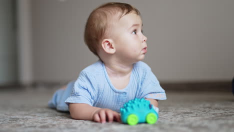 beautiful baby lying on belly on the floor with toy in front of him. cute child looks up and smiles to somebody adorably. blurred backdrop.