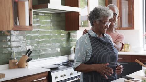 Felices-Amigas-Afroamericanas-Mayores-Poniéndose-Delantal-En-La-Cocina,-Espacio-Para-Copiar,-Cámara-Lenta