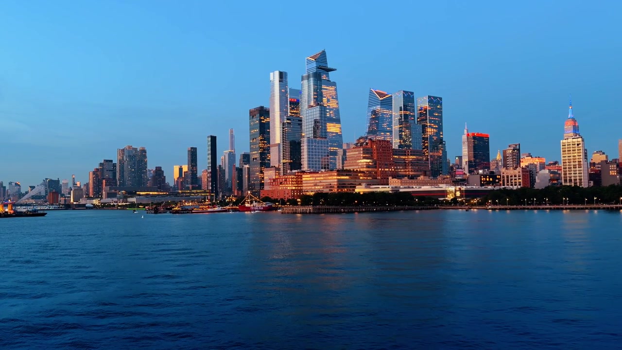 Skyline di Hudson Yards sul fiume Hudson all'ora blu, finestre illuminate e l'Empire State Building in lontananza.