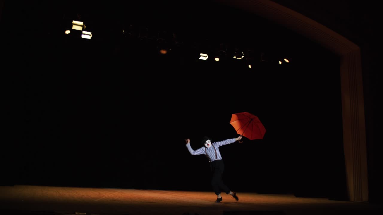 actuación de mimo en el escenario con paraguas rojos