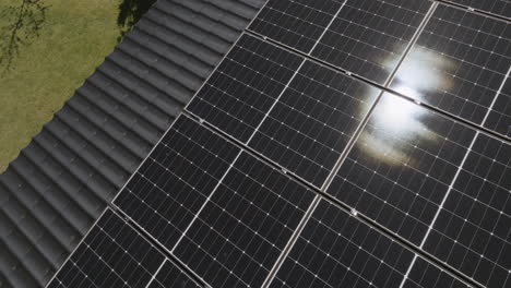 Aerial view rotating on top of mirroring solar cells on a house roof, sunny day