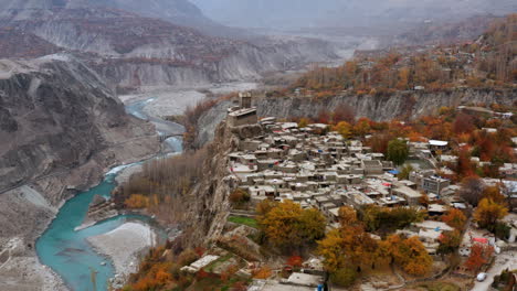 drone shot of altit fort in hunza valley with turquoise river and autumn forest