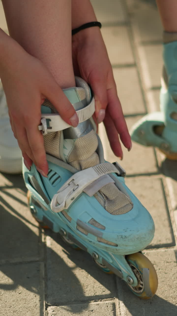 Partial view of individual adjusting roller skate strap on left leg with black wristband under warm sunlight, white sneakers lying nearby on pavement, with greenery softly blurred in background