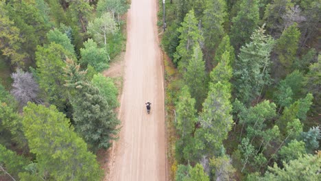 Vista-Aérea-De-Una-Motocicleta-Conduciendo-Por-Un-Camino-De-Tierra-En-Las-Montañas