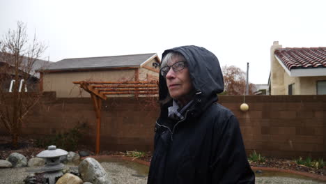 Una-Hermosa-Anciana-Con-Impermeable-Y-Capucha-Parada-Bajo-La-Lluvia-Mirando-Al-Cielo-Sonriendo-Durante-Una-Tormenta-A-Cámara-Lenta