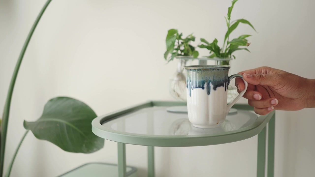 Hand Picking Up a Ceramic Mug from a Minimalist Side Table