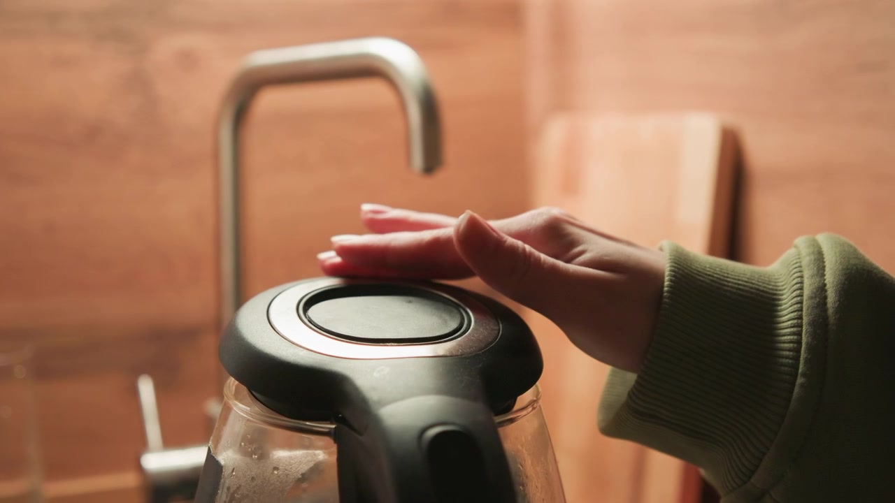 Nahaufnahme einer Hand, die einen Espresso-Siebträger über einer Glaskaraffe hält, mit sichtbarem Deckeldrücken, Aufwärtsheben, nassem Rand und Kondensation im warmen Licht einer Holzküche während der Kaffeezubereitung zu Hause.
