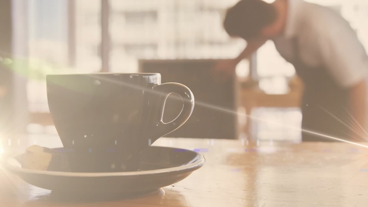 Soft morning light streaming and striking coffee cup on saucer while barista cleaning wooden table