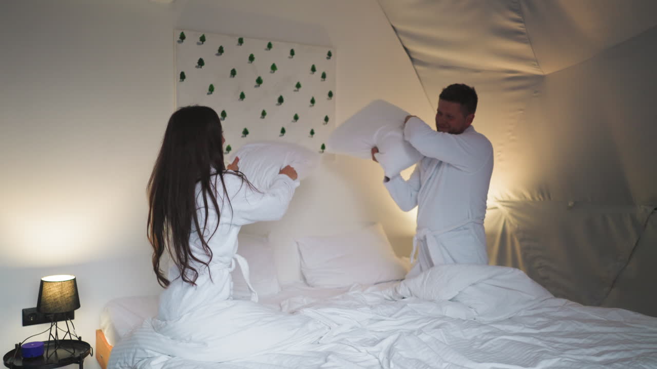 pareja teniendo una pelea de almohadas en una habitación de hotel
