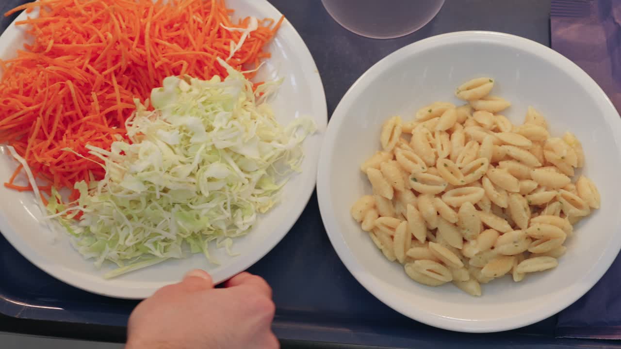 Top-down view of two plates with shredded carrots, cabbage and cooked pasta on serving tray.