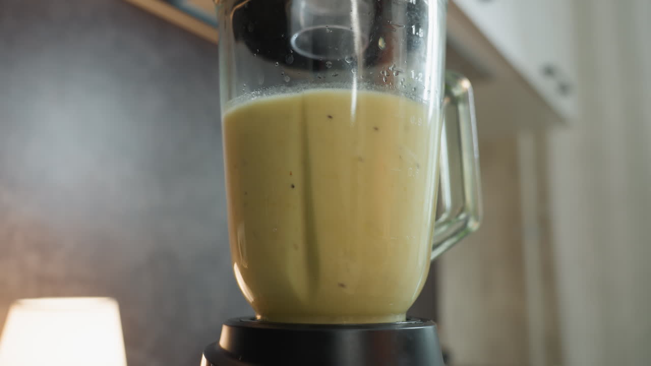 Barattolo del frullatore in primo piano con smoothie, illuminazione calda della cucina, barattolo di vetro riempito con smoothie verde cremoso, bagliore di una lampada sullo sfondo, scena sul bancone della cucina, chef casalingo che prepara una colazione sana, spinaci freschi