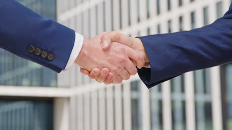 two caucasian business men in suits shake hands outdoors, close-up