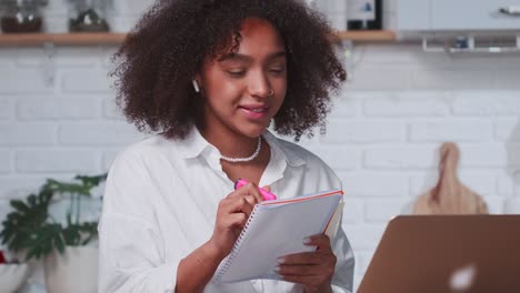 successful african american woman taking notes in notebook while looking in
