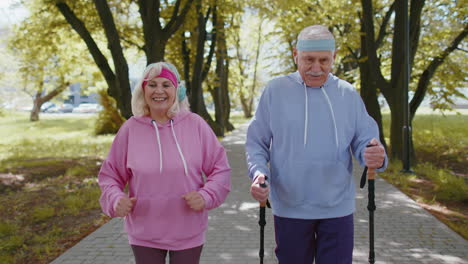 Active-senior-grandparents-training-Nordic-walking-with-ski-trekking-poles,-running-in-summer-park