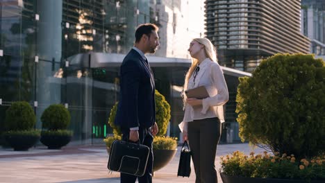 two business people man and woman talking standing outside office building entrance after work - slow motion