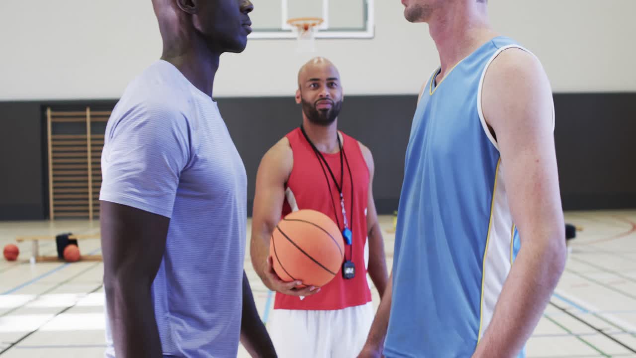 Mangfoldig mannsbasketcoach med ball og lagene stiller opp for kamp på en innendørsbane, i sakte film.