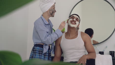 Mujer-Con-Máscara-Facial-Aplicando-Exfoliante-A-Un-Apuesto-Hombre-Negro