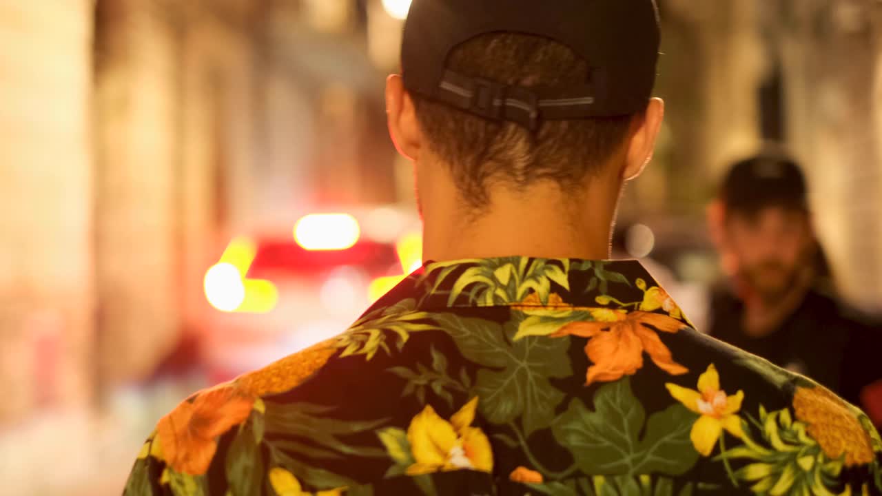 Close Crop Gimbal Rear Following View of Young Tan Man with Black Hat and Hawaiin Shirt Walking Through Crowded Street at Night