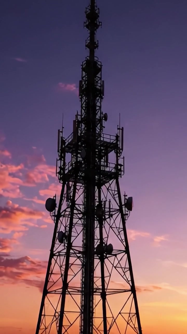 Una struttura imponente contro un cielo al tramonto colorato: la trasformazione di una torre di comunicazione mentre il giorno si trasforma in notte.