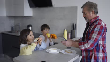 Two-small-children-are-eating-sandwiches-made-by-grandfather,-slow-motion