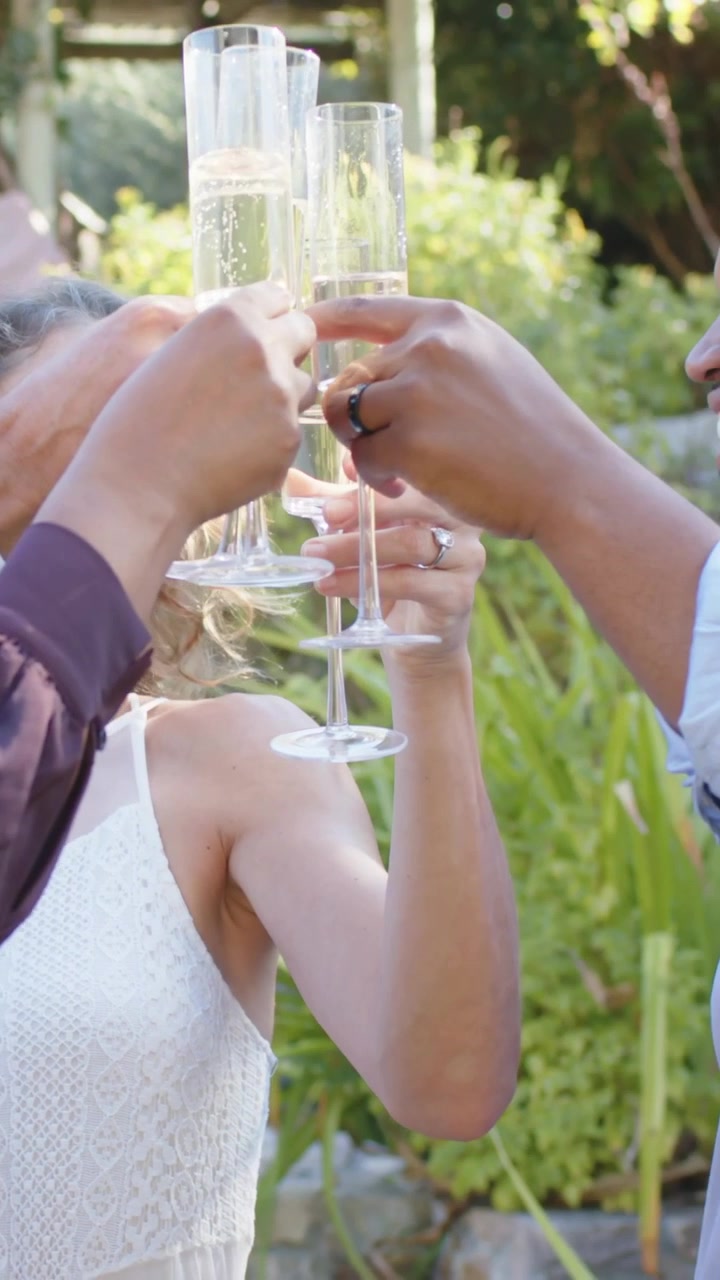 Vertical video: Groom leading toast bride in lace lifting glasses in garden toasting couple, flutes