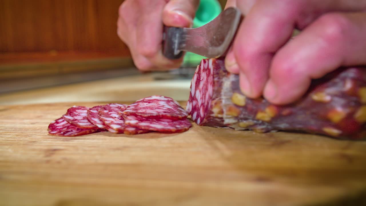 las manos sostienen el salami mientras se cortan en rodajas en una tabla de cortar de madera