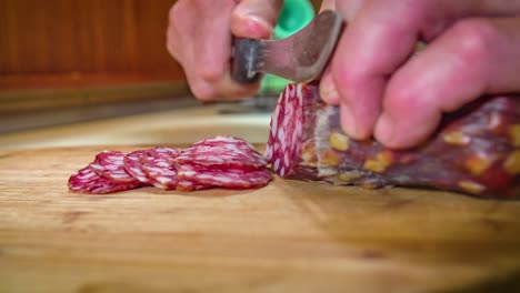 les mains tiennent le salami tout en étant découpées en tranches sur une planche à découper en bois