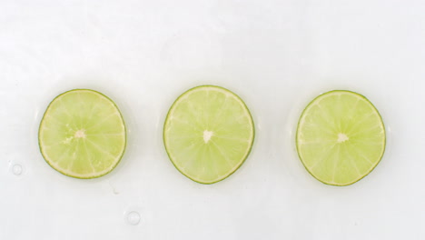 water splashes in slow motion. top view: three slices of green lime washed by water on a white background