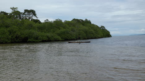 static shot of a local panamanian rowing in a small boat looking for fish in the water near the jungle