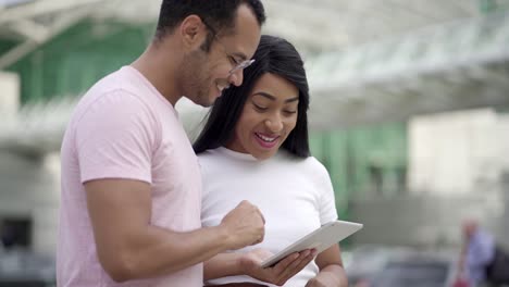 Joyful-friends-standing-on-street-and-using-tablet