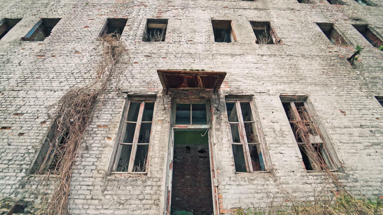 Abandoned building with broken windows in the war. Damaged brick three-storeyed building outside. Camera moves back.