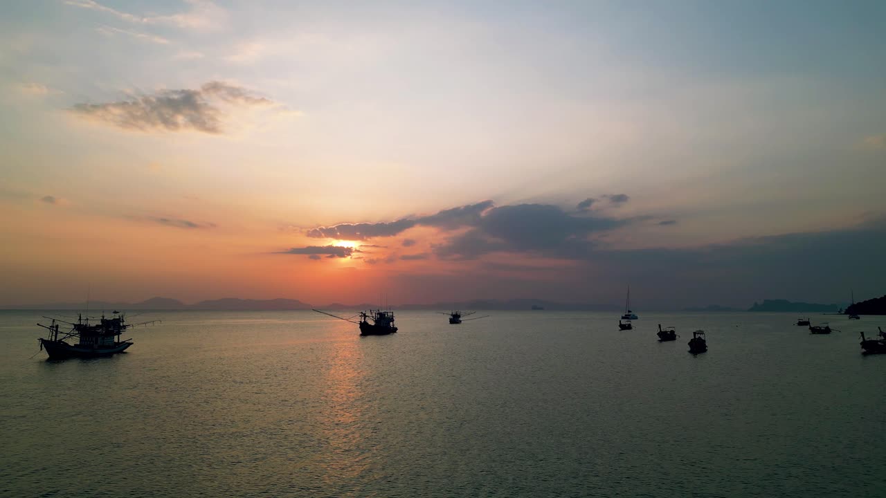 Peaceful sunset over the sea in Krabi, Thailand, with traditional fishing boats and silhouettes against the colorful sky