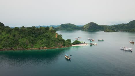 drone footage captures a group of boats sailing around the small islands of komodo national park, with the graceful blue ocean blending seamlessly with the lush green hills of the islands
