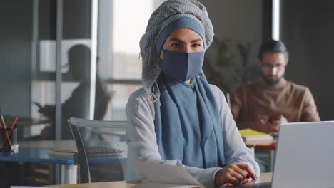 businesswoman in hijab and mask posing for camera at work