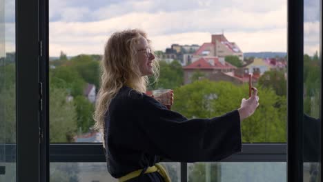 smiling woman stands in balcony and chats with her family through phone