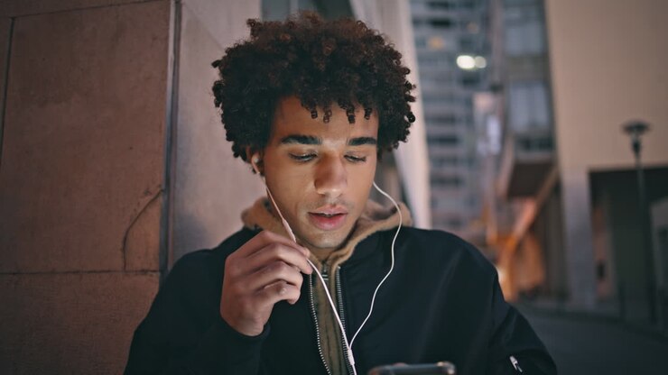 Uomo rilassato che parla al suo smartphone usando le cuffie nel crepuscolo urbano, primo piano.