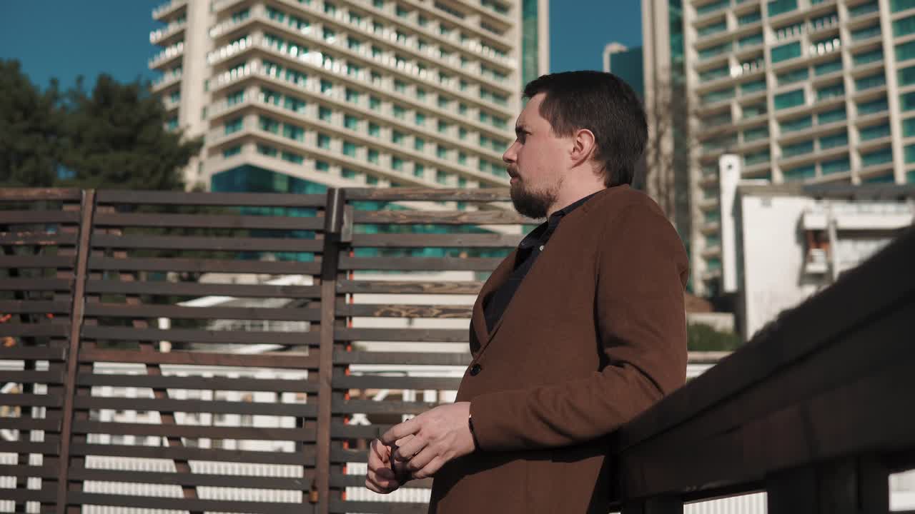 hombre de chaqueta marrón por una valla de la ciudad