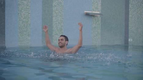 hombre joven y feliz salpicando agua en una lujosa piscina