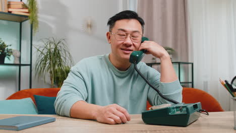 Asian-man-making-retro-telephone-from-90s-conversation-call-with-friends-on-couch-at-home-in-room