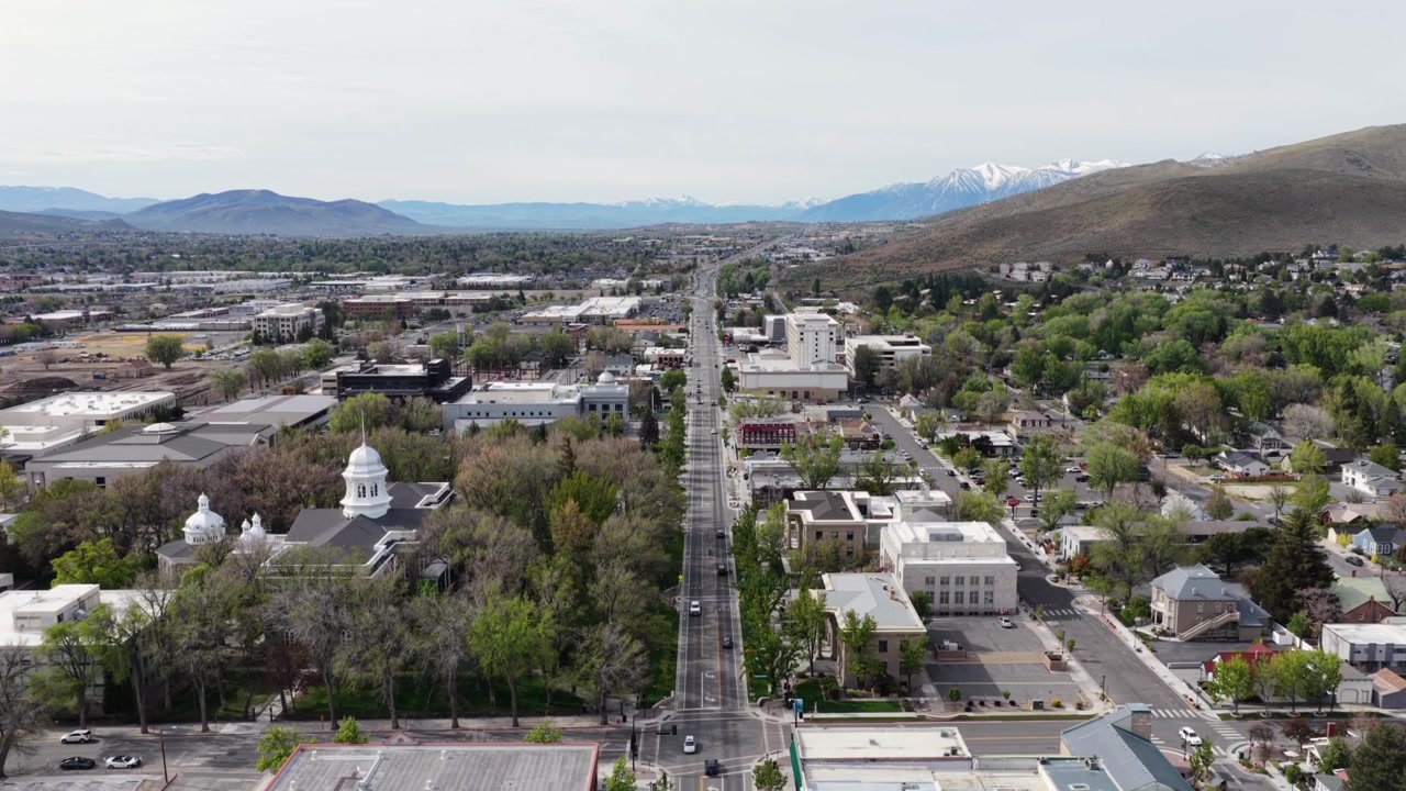 Centro di Carson City, Nevada, con la cupola del Campidoglio dello Stato del Nevada e una lunga strada dritta che conduce verso le montagne della Sierra Nevada coperte di neve, sotto un cielo limpido e luminoso durante una soleggiata mattina di primavera. Discesa aerea.