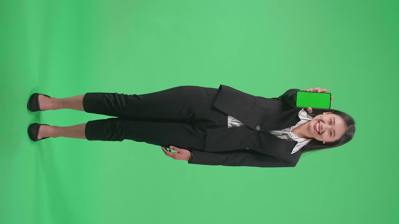 Full Body Of An Asian Business Woman With A Smile Showing Green Screen Mobile Phone While Standing In Front Of Green Screen